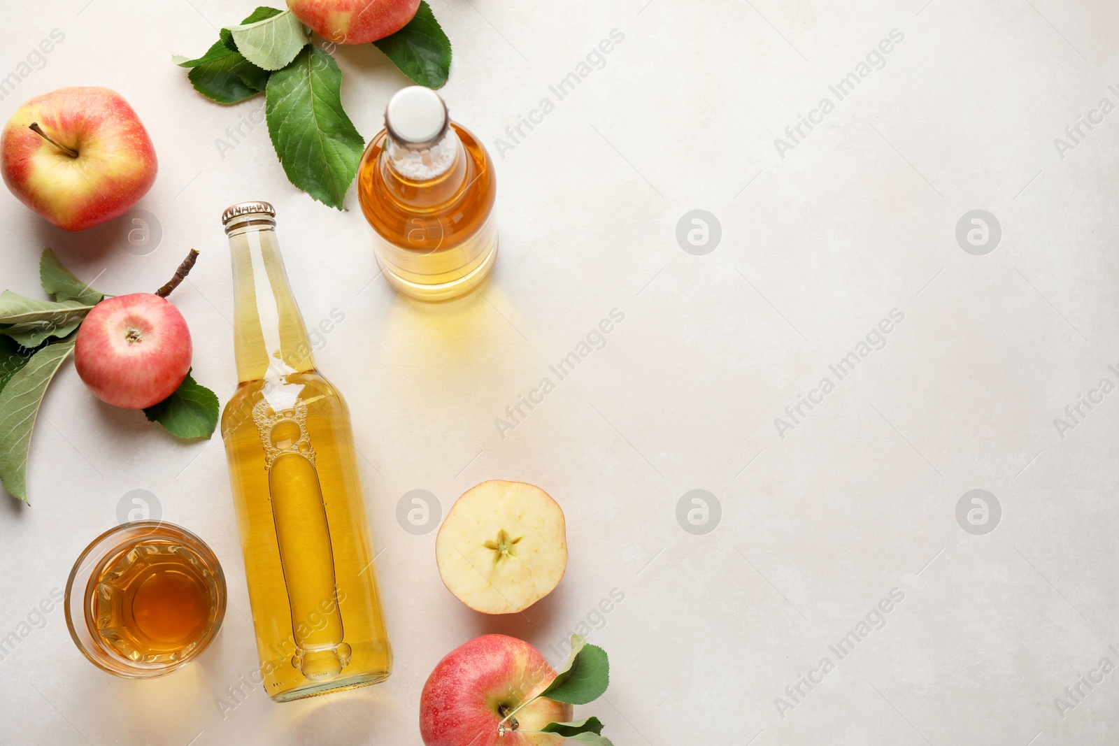 Photo of Delicious cider in bottles, glass and apples with green leaves on beige table, flat lay. Space for text