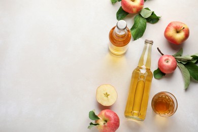 Photo of Delicious cider in bottles, glass and apples with green leaves on beige table, flat lay. Space for text