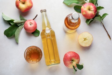 Photo of Delicious cider in bottles, glass and apples with green leaves on light table, flat lay