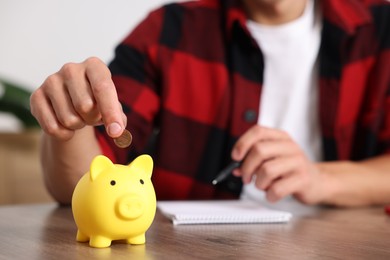 Photo of Man planning budget and putting money into piggy bank at wooden table, selective focus