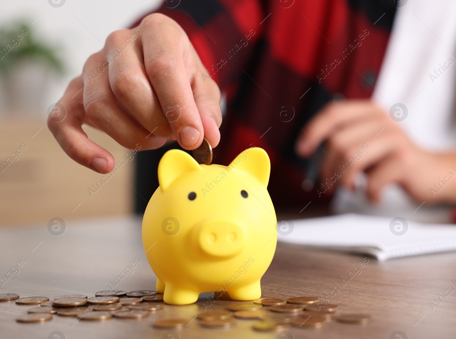 Photo of Man planning budget and putting money into piggy bank at wooden table, selective focus