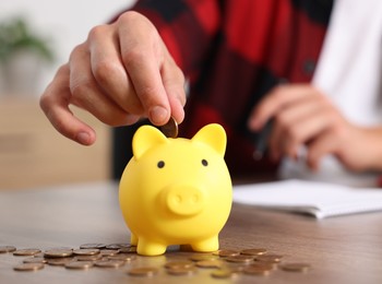 Photo of Man planning budget and putting money into piggy bank at wooden table, selective focus