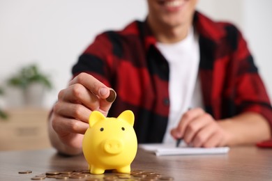 Photo of Man planning budget and putting money into piggy bank at wooden table, selective focus