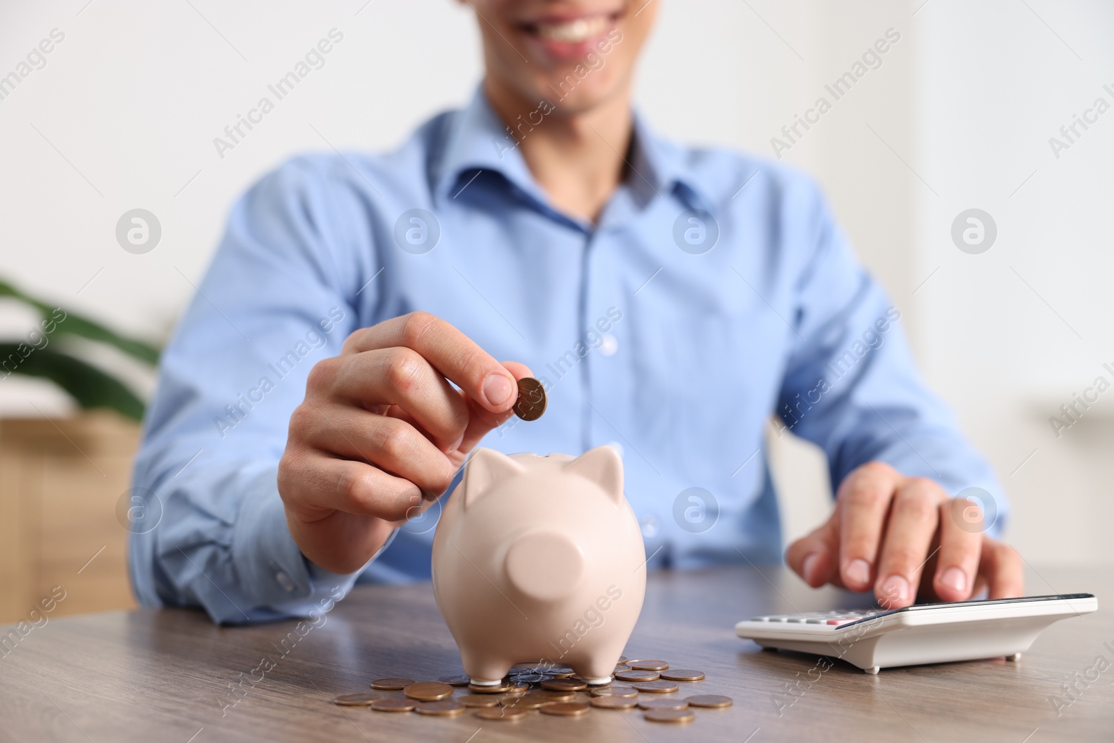 Photo of Man putting money into piggy bank at wooden table, closeup
