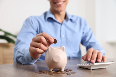 Photo of Man putting money into piggy bank at wooden table, closeup