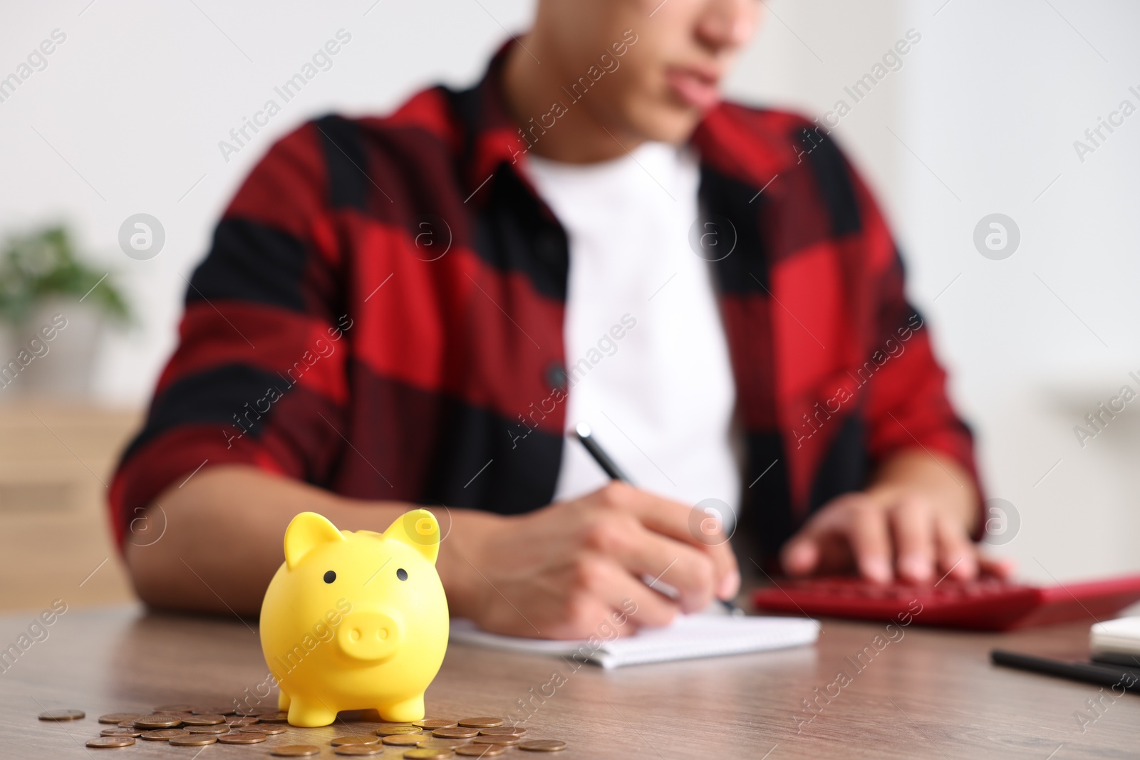 Photo of Piggy bank with coins on wooden table and man planning budget, selective focus