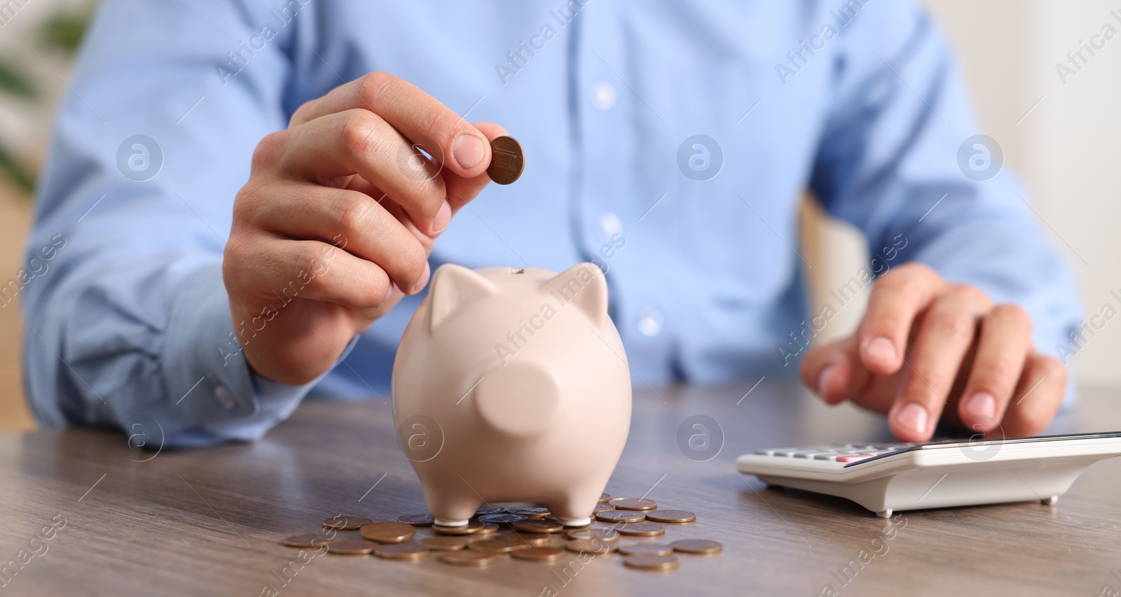 Photo of Man putting money into piggy bank at wooden table, closeup