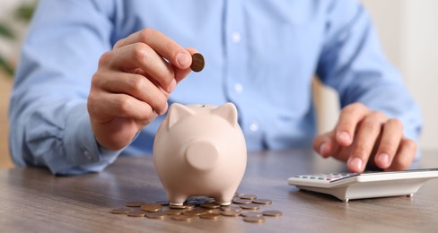 Photo of Man putting money into piggy bank at wooden table, closeup