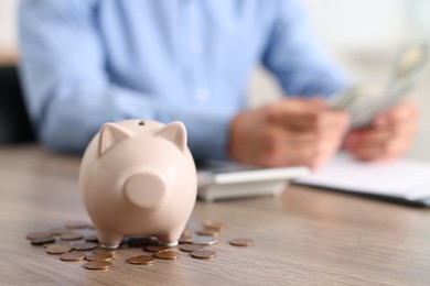 Photo of Piggy bank with coins on wooden table and man planning budget, selective focus