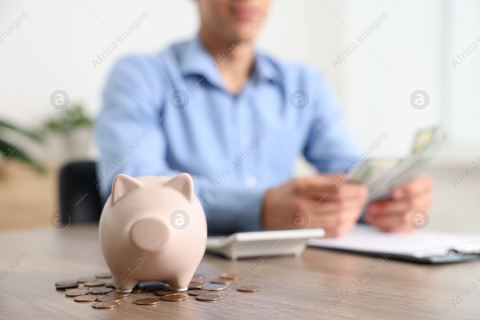 Photo of Piggy bank with coins on wooden table and man planning budget, selective focus