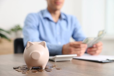 Photo of Piggy bank with coins on wooden table and man planning budget, selective focus
