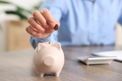 Photo of Man putting money into piggy bank at wooden table, closeup