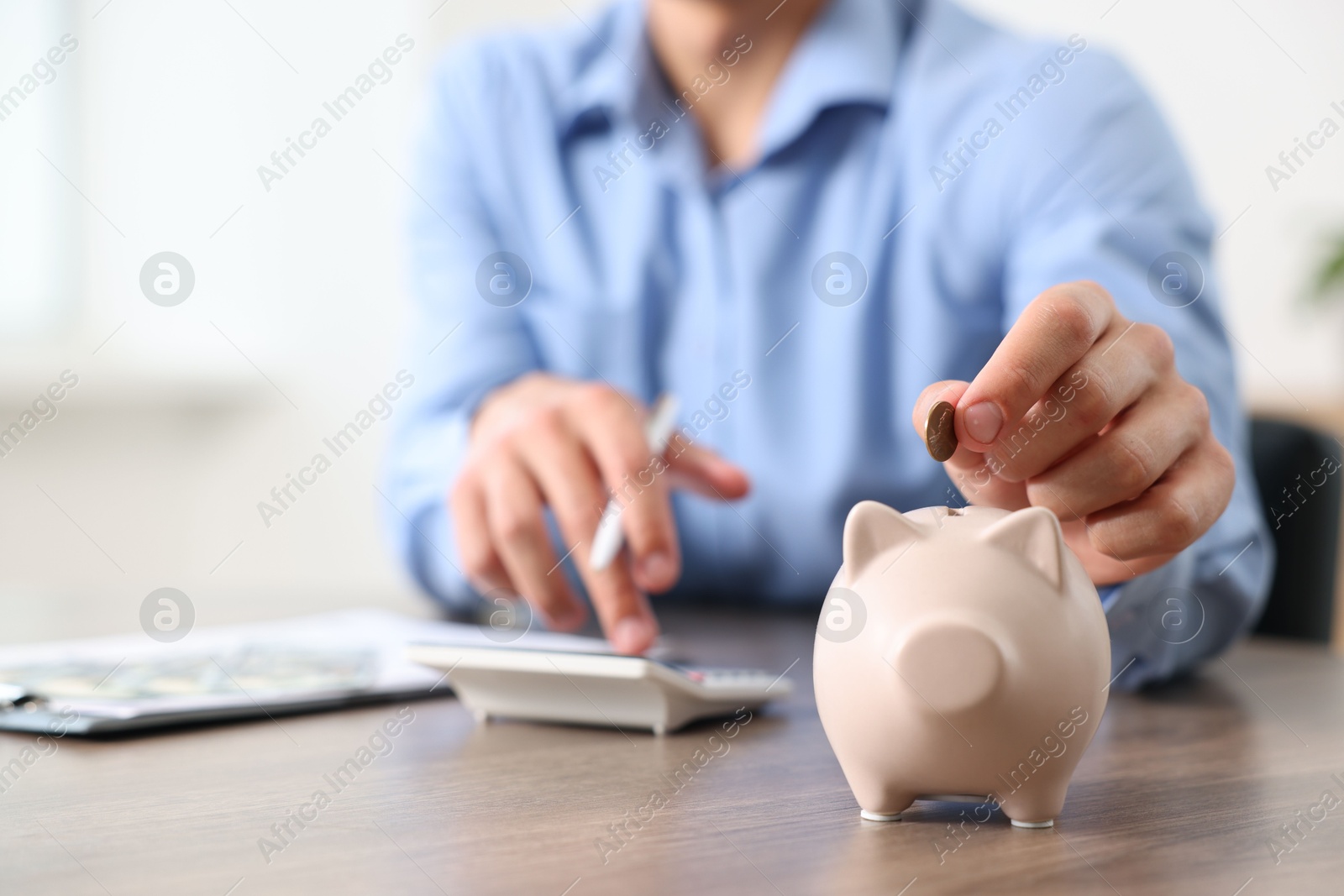 Photo of Man planning budget and putting money into piggy bank at wooden table, selective focus