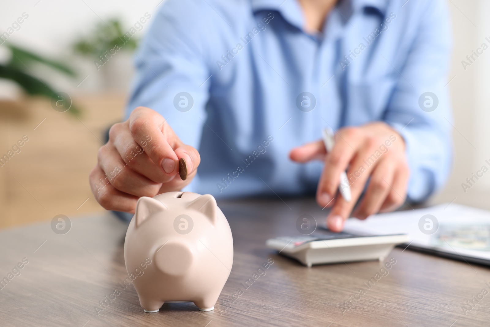 Photo of Man planning budget and putting money into piggy bank at wooden table, selective focus