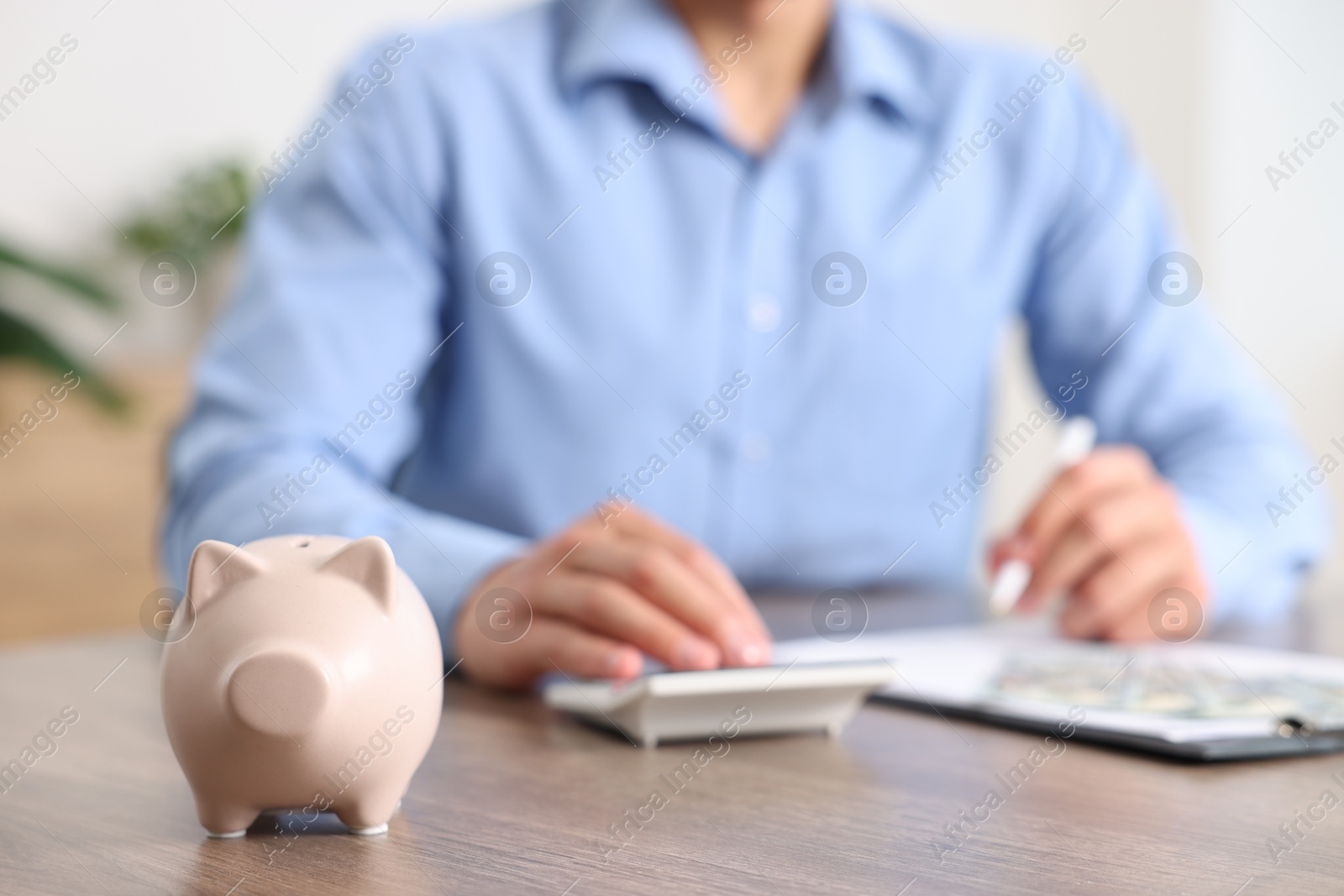 Photo of Piggy bank on wooden table and man planning budget, selective focus