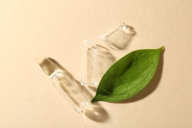 Photo of Glass ampoules with cosmetic product, leaf and water drops on beige background, flat lay