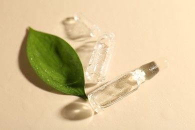 Photo of Glass ampoules with cosmetic product, leaf and water drops on beige background, closeup