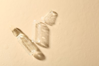 Photo of Glass ampoules with cosmetic product and water drops on beige background, flat lay. Space for text