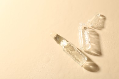 Photo of Glass ampoules with cosmetic product and water drops on beige background, flat lay. Space for text