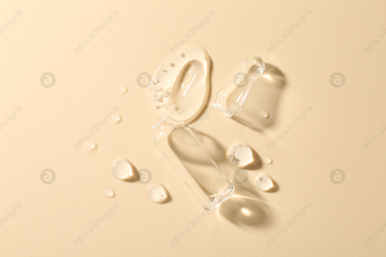 Broken glass ampoule and cosmetic product on beige background, top view Photo of Broken glass ampoule and cosmetic product on beige background, top view