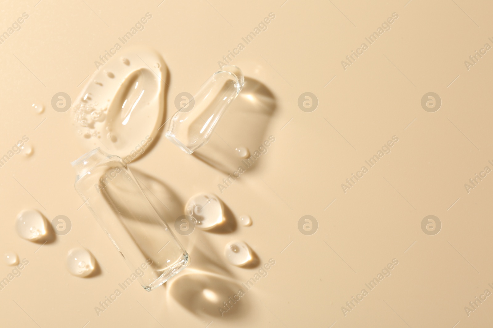 Photo of Broken glass ampoule and cosmetic product on beige background, top view