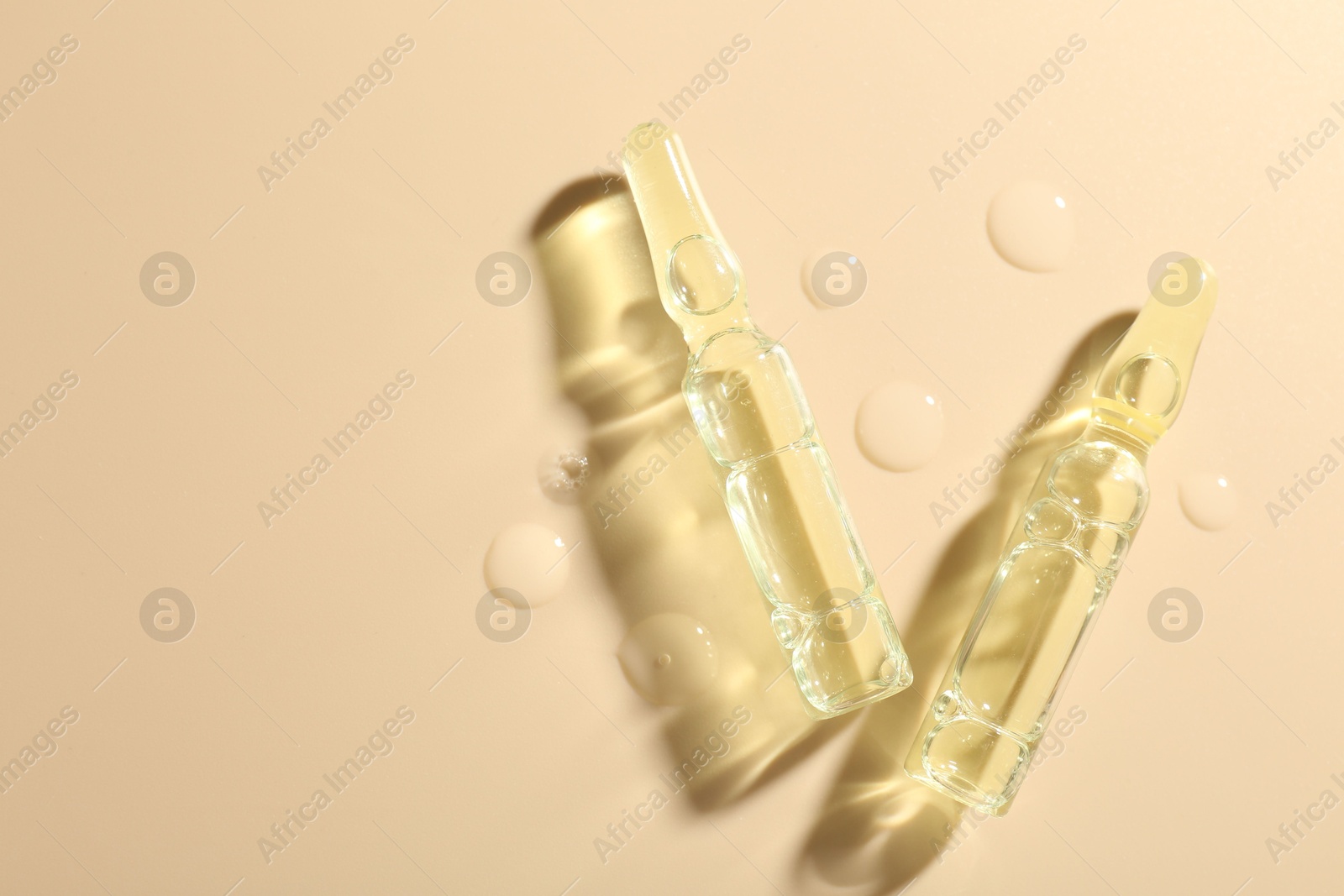 Photo of Glass ampoules with cosmetic product and water drops on beige background, flat lay. Space for text