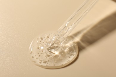 Photo of Taking cosmetic product with pipette on beige background, closeup