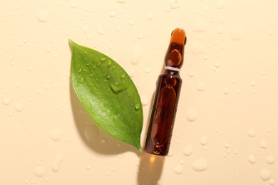 Photo of Glass ampoule with cosmetic product, leaf and water drops on beige background, flat lay