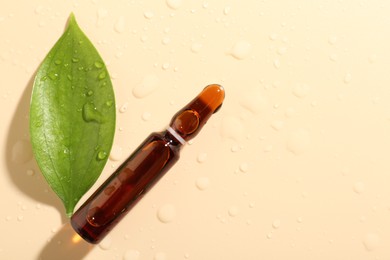 Photo of Glass ampoule with cosmetic product, leaf and water drops on beige background, flat lay. Space for text