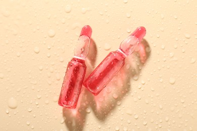 Photo of Glass ampoules with cosmetic product and water drops on beige background, top view