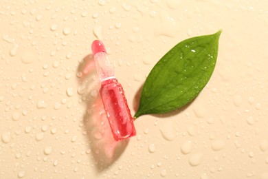 Photo of Glass ampoule with cosmetic product, leaf and water drops on beige background, flat lay