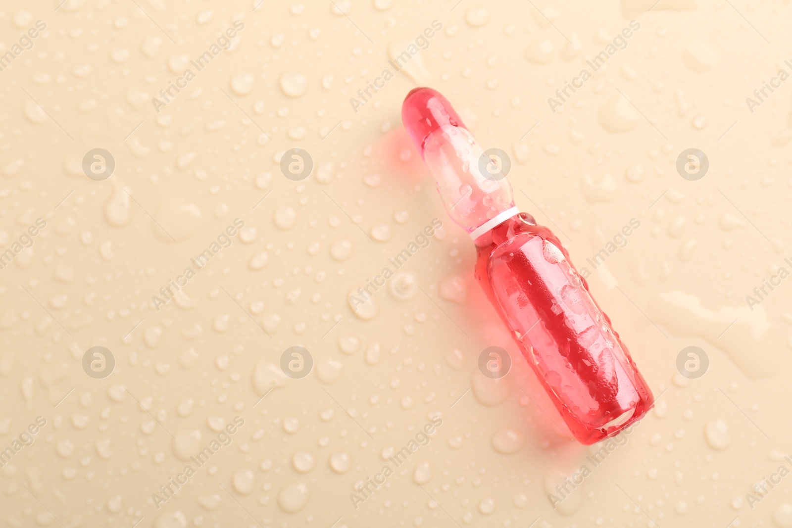 Photo of Glass ampoule with cosmetic product and water drops on beige background, top view. Space for text