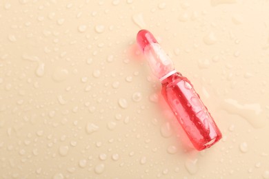 Photo of Glass ampoule with cosmetic product and water drops on beige background, top view. Space for text