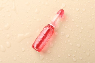 Photo of Glass ampoule with cosmetic product and water drops on beige background, top view