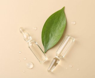 Photo of Glass ampoules with cosmetic product, leaf and water drops on beige background, flat lay