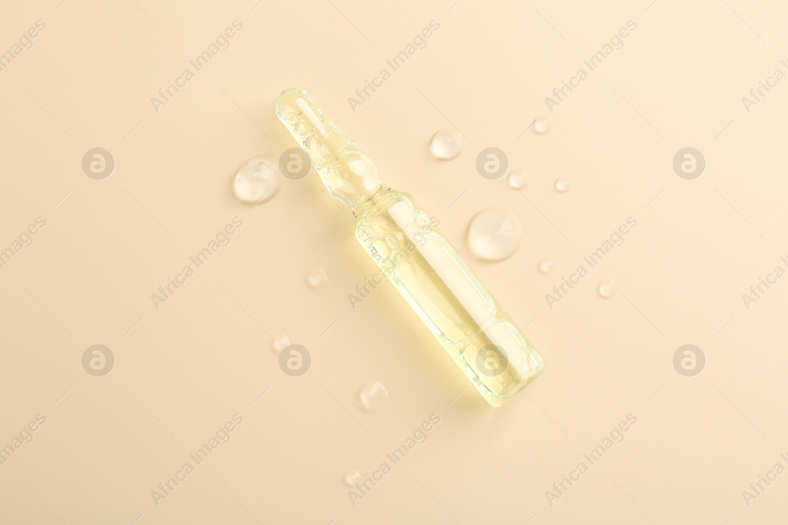Photo of Glass ampoule with cosmetic product and water drops on beige background, top view