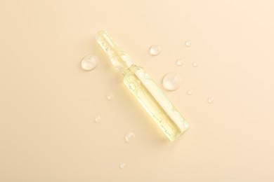 Photo of Glass ampoule with cosmetic product and water drops on beige background, top view