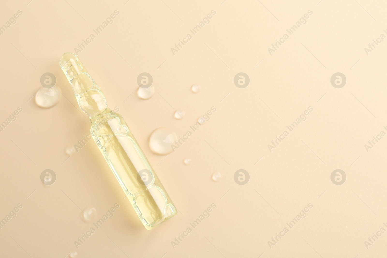 Photo of Glass ampoule with cosmetic product and water drops on beige background, top view. Space for text
