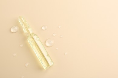 Photo of Glass ampoule with cosmetic product and water drops on beige background, top view. Space for text