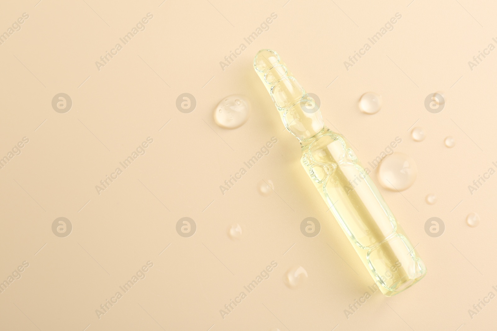 Photo of Glass ampoule with cosmetic product and water drops on beige background, top view. Space for text