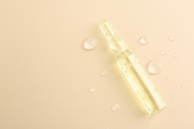 Photo of Glass ampoule with cosmetic product and water drops on beige background, top view. Space for text
