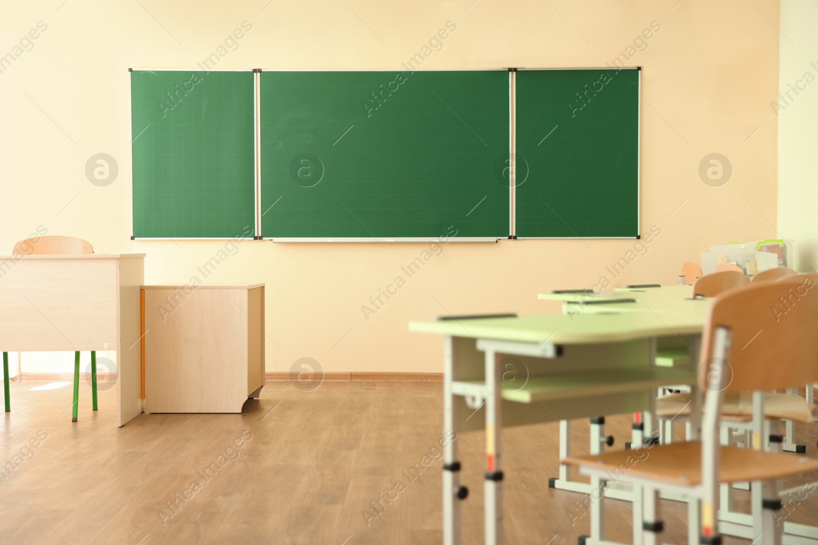 Photo of Desks with chairs and green chalkboard in classroom