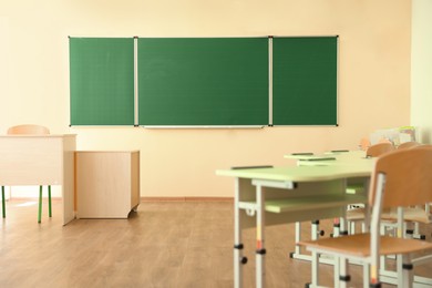 Photo of Desks with chairs and green chalkboard in classroom