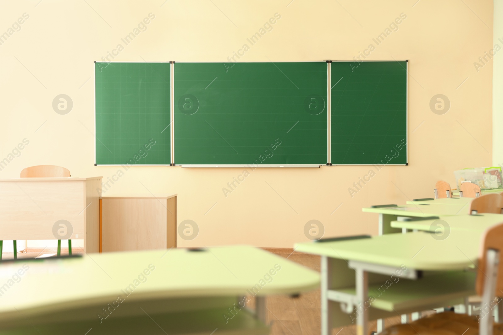 Photo of Desks with chairs and green chalkboard in classroom
