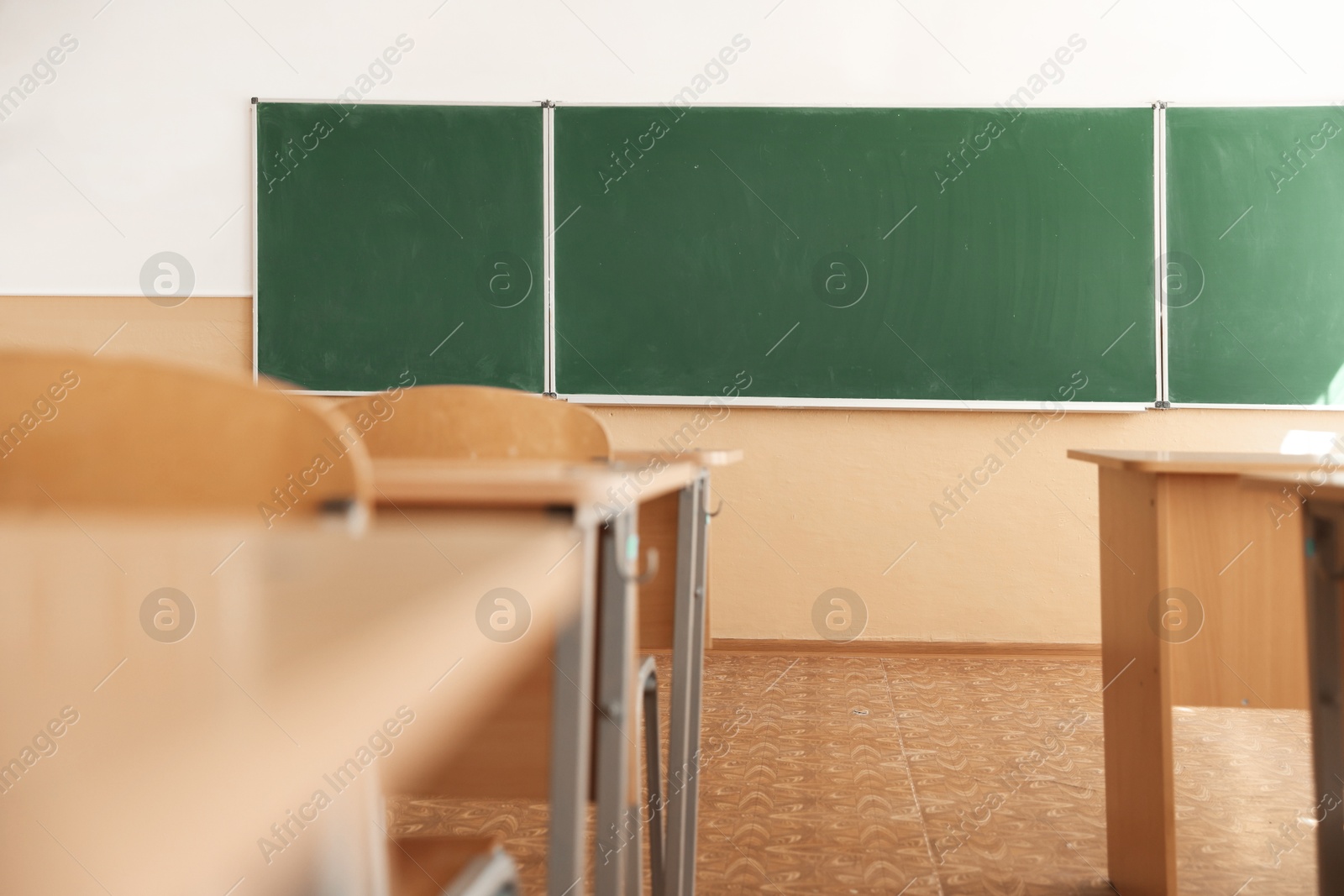Photo of Desks with chairs and green chalkboard in classroom