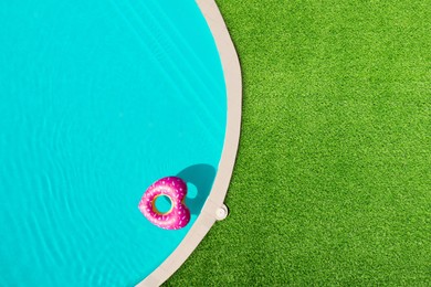 Image of Heart shaped inflatable ring floating in swimming pool surrounded by green grass, top view