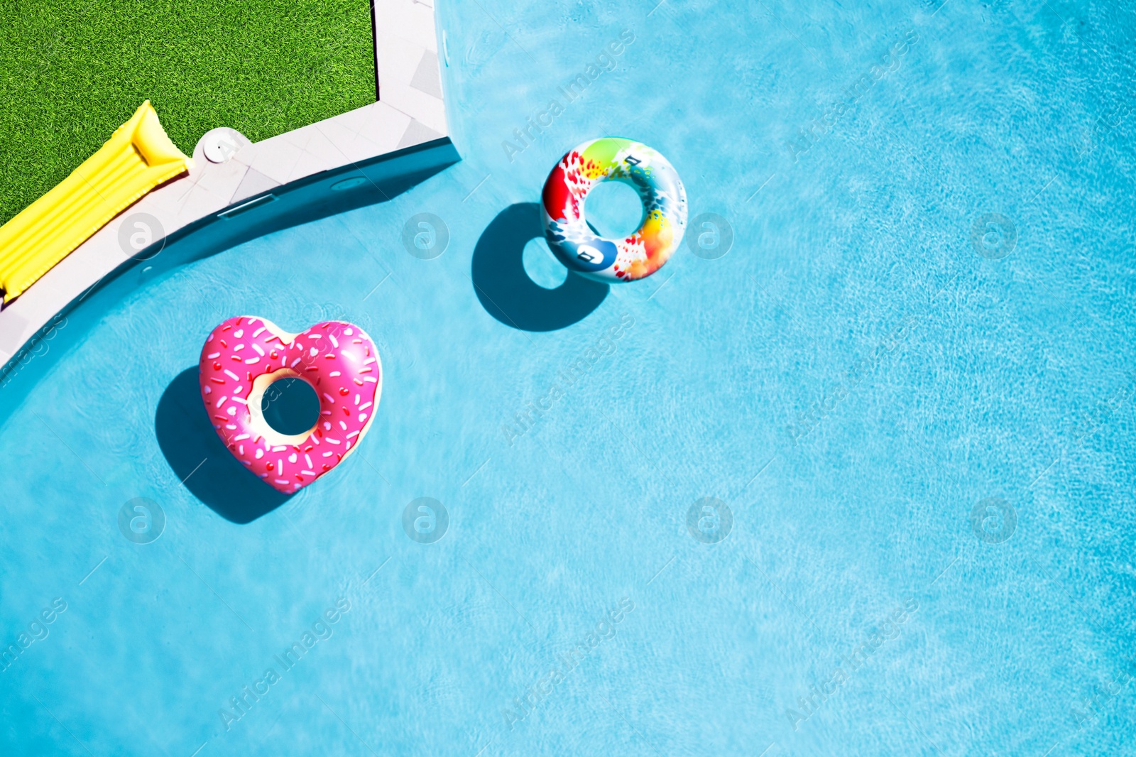 Inflatable rings floating in swimming pool surrounded by green grass, top view Image of Inflatable rings floating in swimming pool surrounded by green grass, top view