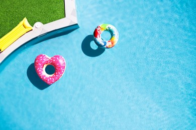 Image of Inflatable rings floating in swimming pool surrounded by green grass, top view