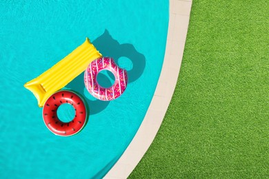 Image of Inflatable rings and mattress floating in swimming pool surrounded by green grass, top view