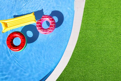 Image of Inflatable rings and mattress floating in swimming pool surrounded by green grass, top view